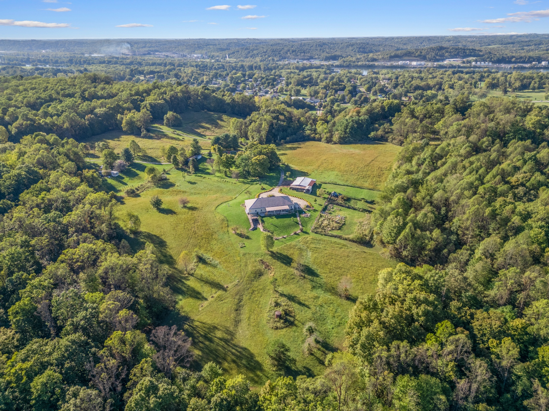 Wide aerial of countryside property with home, pasture, and forested hills overlooking the river valley
