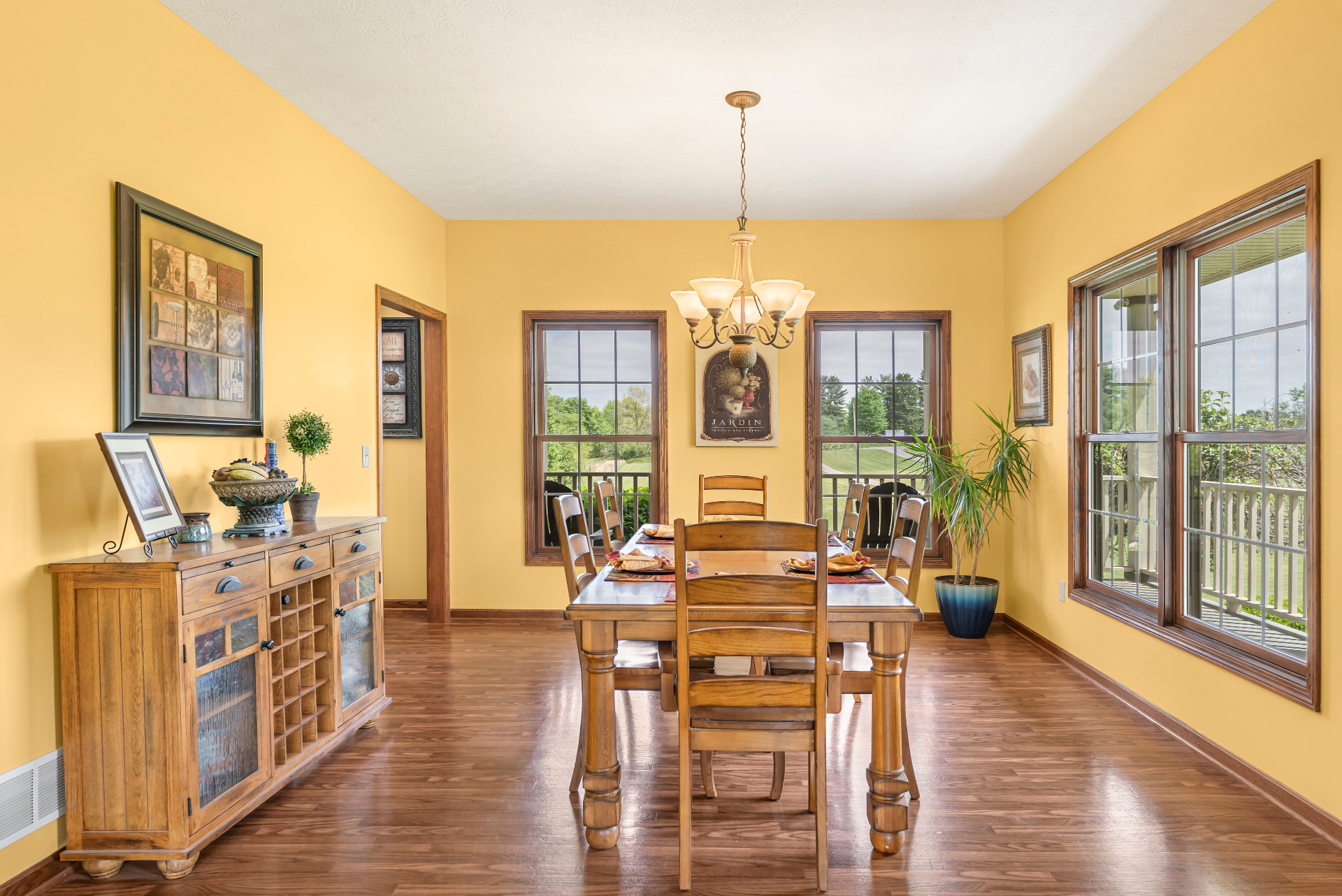 Warm yellow dining room with wood table, chandelier, and large windows